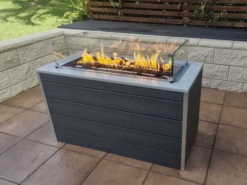 Gas fire pit with glass wind guard and tall flames on a stamped concrete Brisbane patio