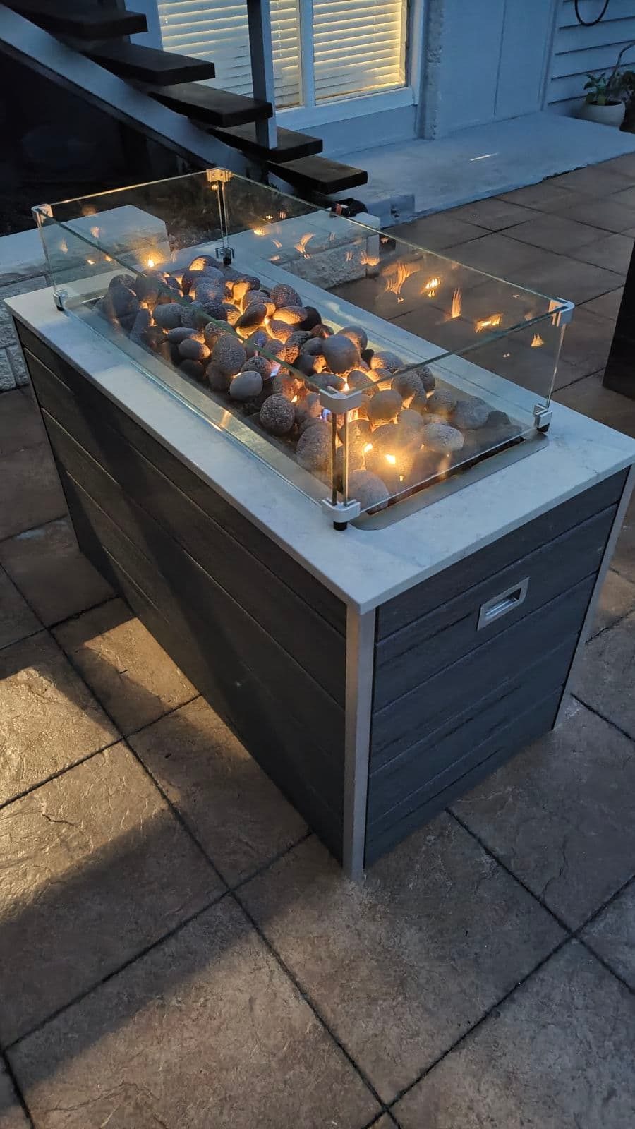 Outdoor gas fire pit lit at dusk on a Brisbane patio beside timber stairs